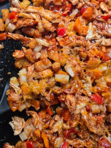 Gluten-free BBQ chicken totchos on a baking sheet topped with crispy tater tots, shredded chicken, barbecue sauce, melted cheese.