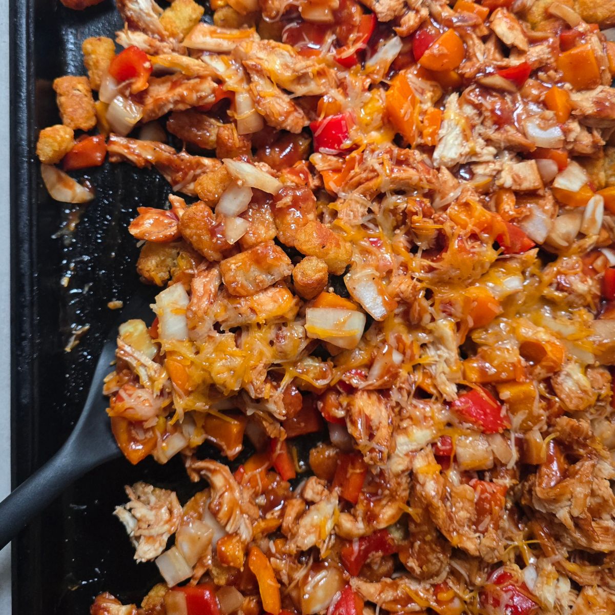 Gluten-free BBQ chicken totchos on a baking sheet topped with crispy tater tots, shredded chicken, barbecue sauce, melted cheese.