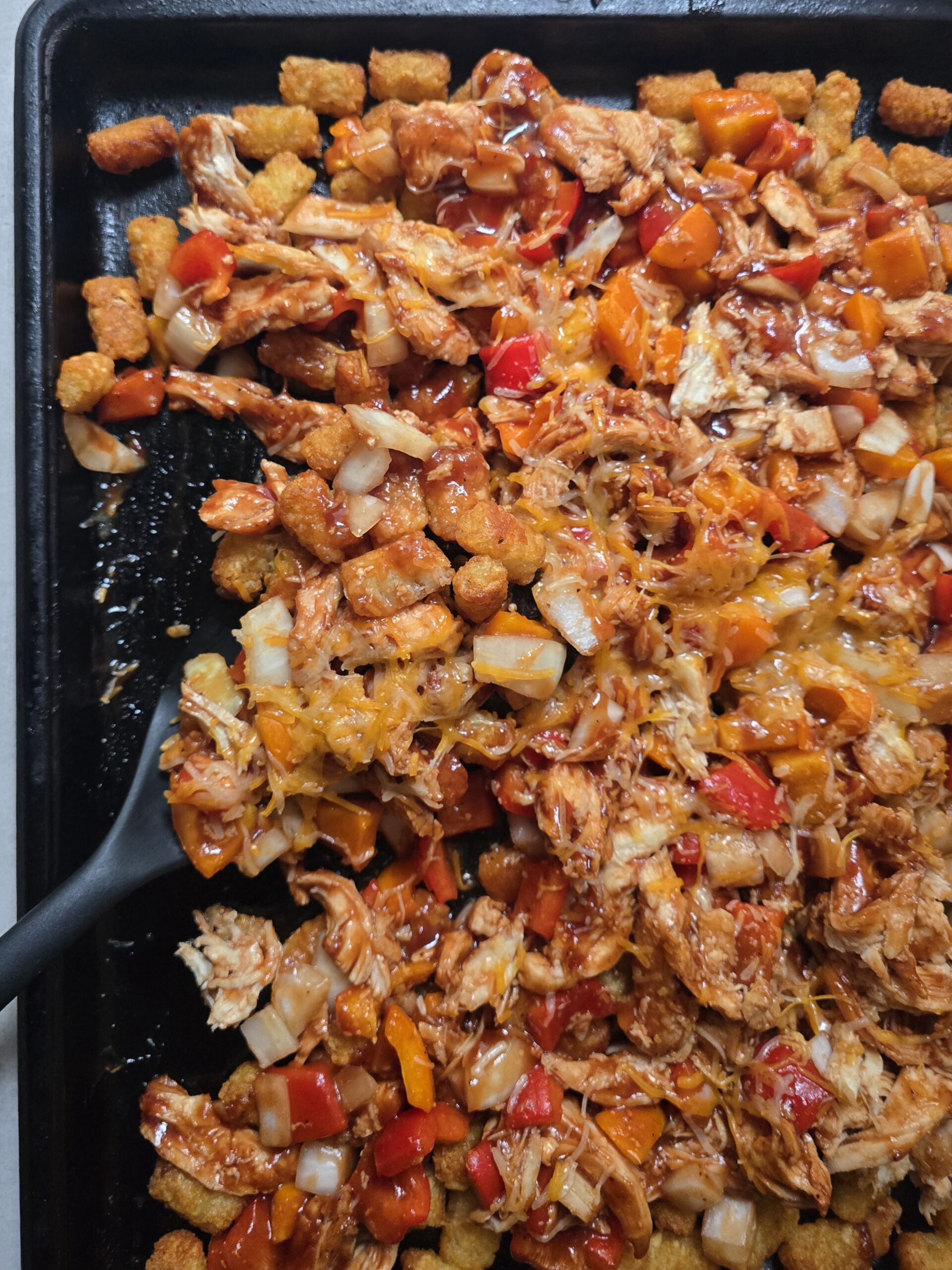 Overhead view of homemade BBQ chicken totchos on a baking sheet with crispy tater tots, barbecue chicken,  pepper, onions and melted cheddar cheese,
