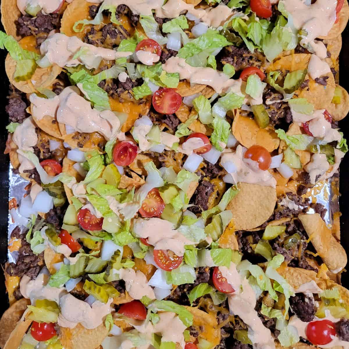 Big Mac nachos with homemade special sauce being drizzled over melted cheese and seasoned beef