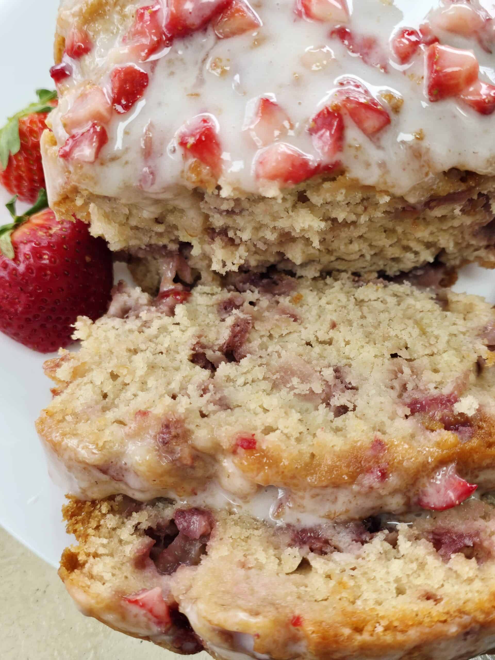 Gluten free strawberry bread with sweet frosting sliced on a plate showing fresh strawberry pieces inside the moist loaf.