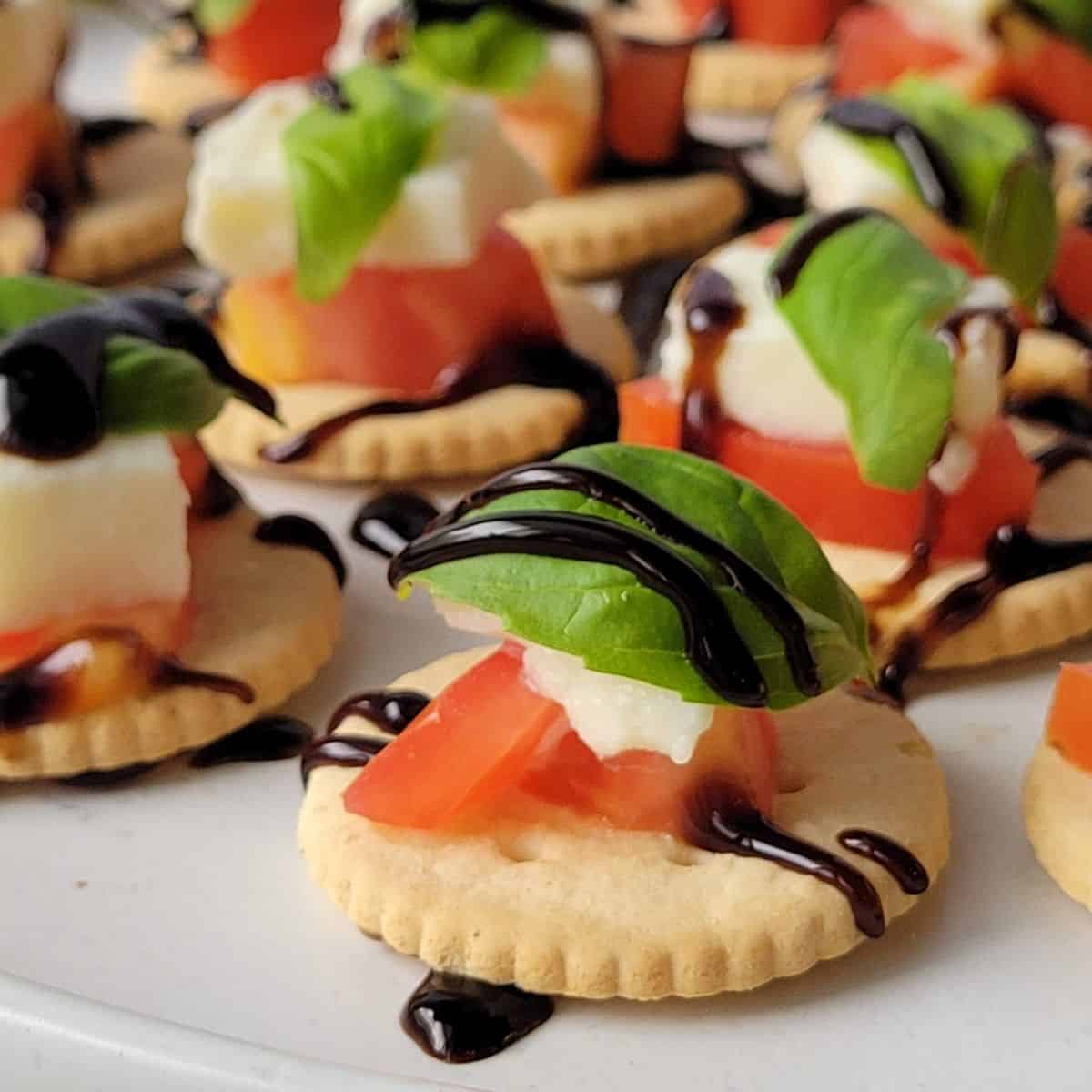 Gluten free caprese cracker stacks with tomatoes and fresh mozzarella drizzled with balsamic glaze on a serving tray.