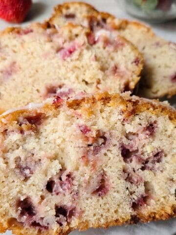 Close up of moist gluten free strawberry bread slices topped with strawberry glaze and filled with fresh strawberries.