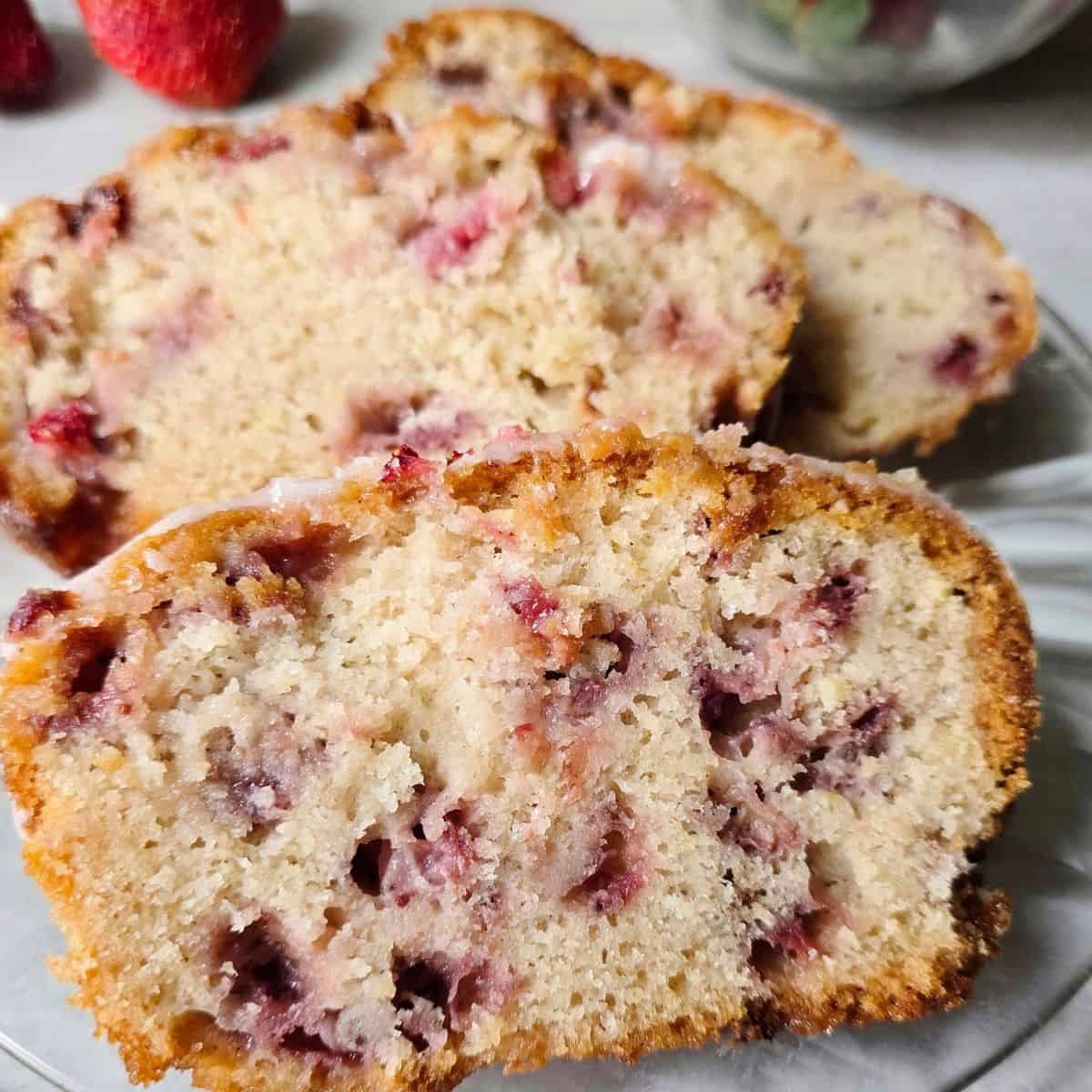 Close up of moist gluten free strawberry bread slices topped with strawberry glaze and filled with fresh strawberries.