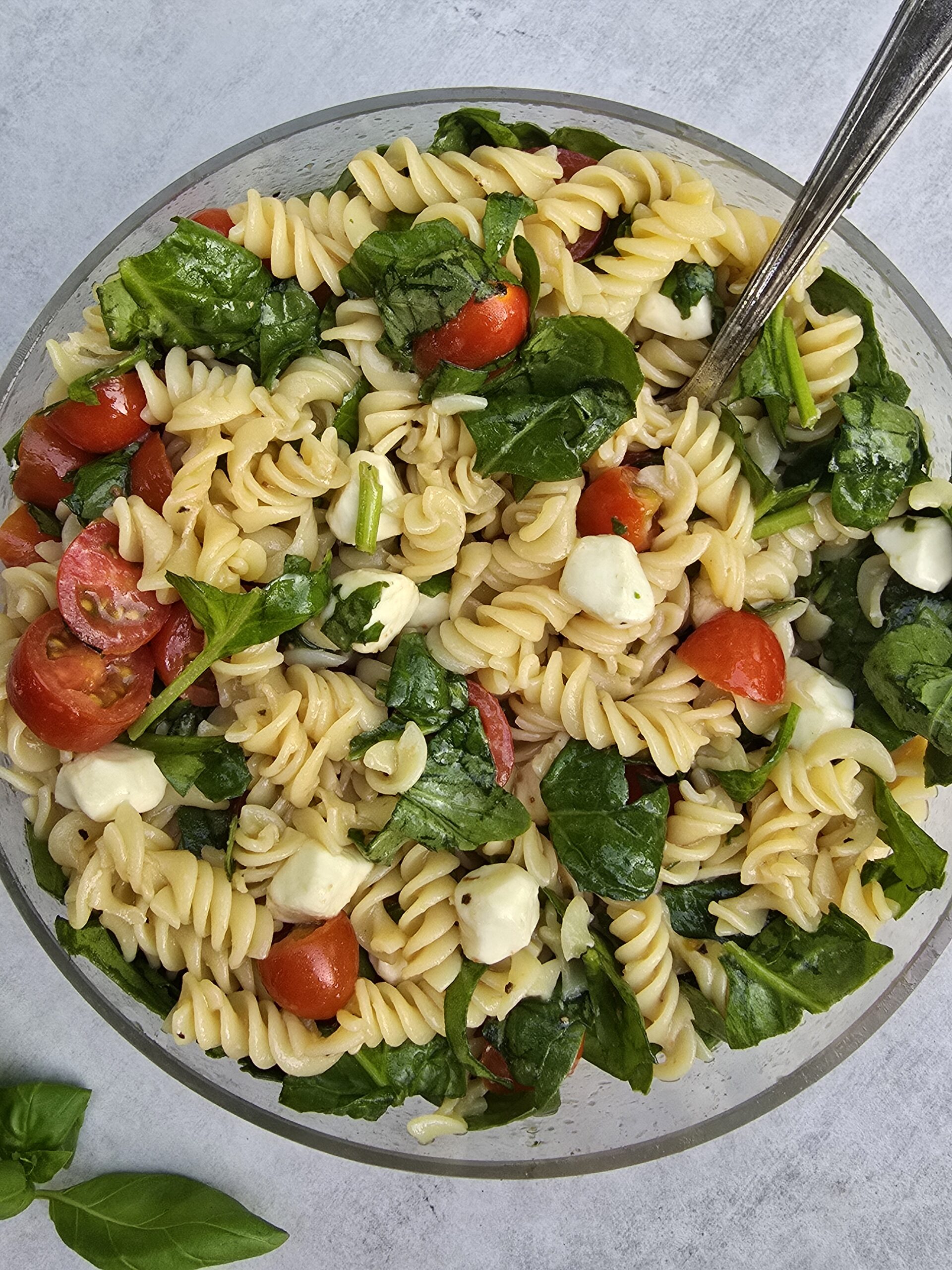 Gluten free caprese pasta salad with spinach, basil, mozzarella, and balsamic dressing in a bowl