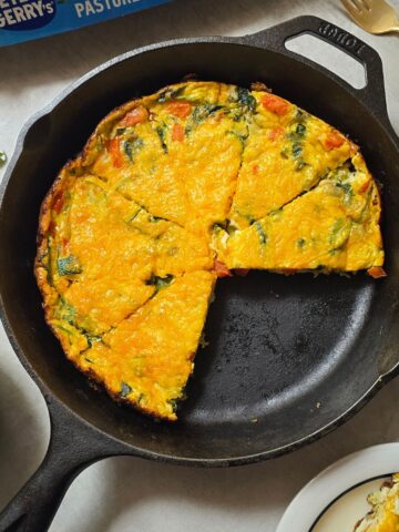 Freshly baked veggie frittata made with zucchini, red pepper, onion, basil, spinach and melted cheese in a cast iron skillet.