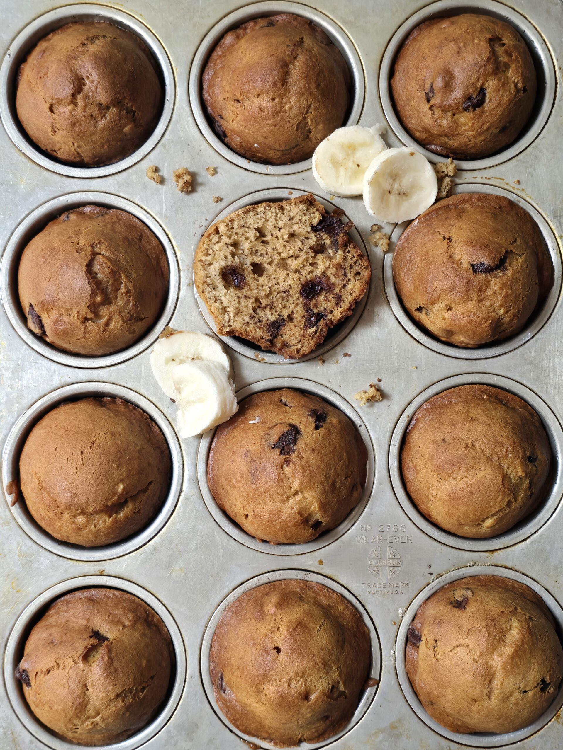 Freshly baked homemade gluten free banana muffins in a muffin pan with golden brown tops.