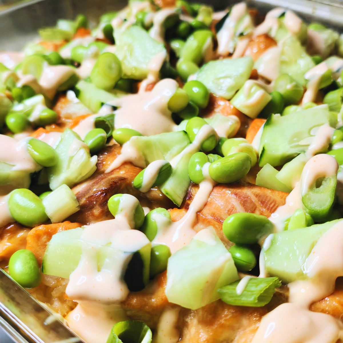 Gluten free salmon sushi bake topped with cucumber, edamame, avocado, green onions and spicy mayo